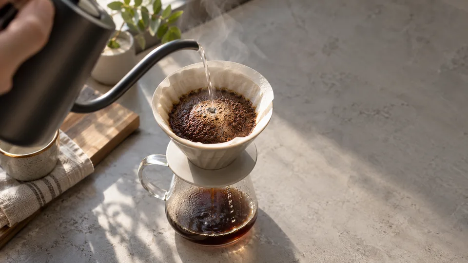 A kettle sends a thin stream of water into a pour-over dripper above a glass server.