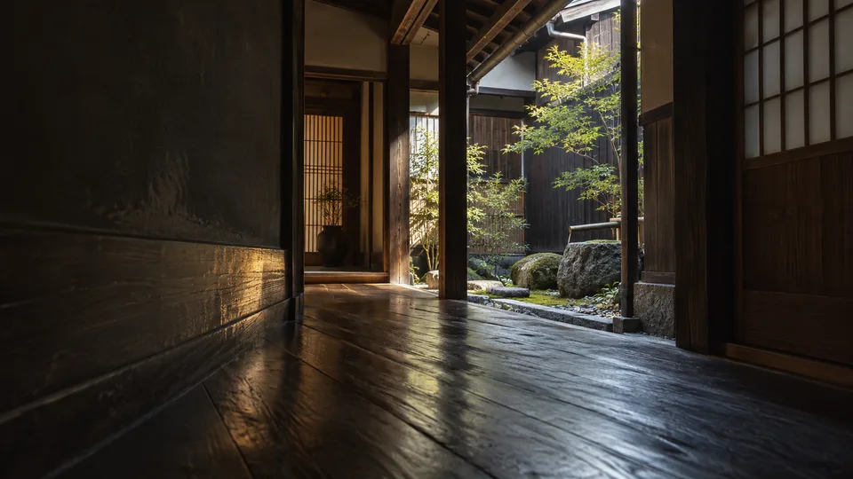 A narrow wooden passage leads toward a small inner courtyard in an anonymous machiya-style guesthouse.