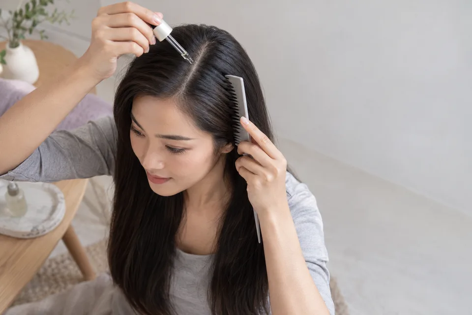 A woman applies a small drop of unbranded scalp serum to a neat hair part.