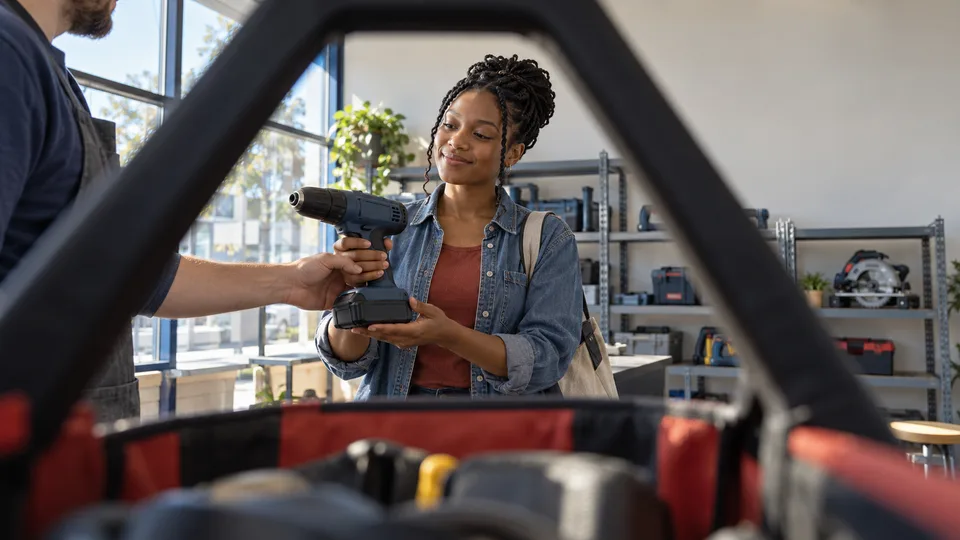 A young woman receives a power drill across a tool case at a lending workshop.